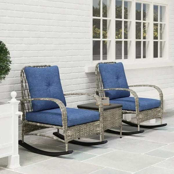 gray rattan chaise lounge chairs with blue cushions and black rocking bases by a white brick wall