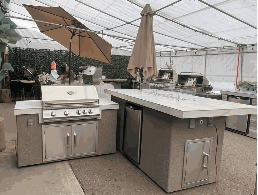 modern outdoor BBQ island with built-in grill, refrigerator, bar counter, fire pit, and umbrellas in a showroom