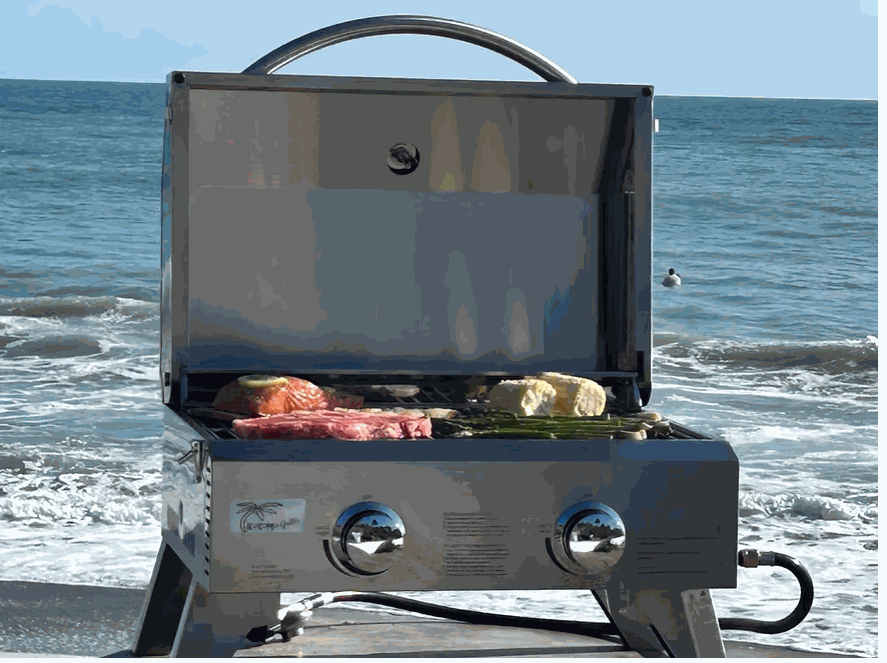 KoKoMo Portable Grill stainless steel tabletop BBQ grilling steak and vegetables on the beach with ocean background