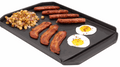 Cast iron plancha griddle cooking bacon, sausages, eggs, and potatoes with tall sides and grease trough designed for Broil King BBQ grills