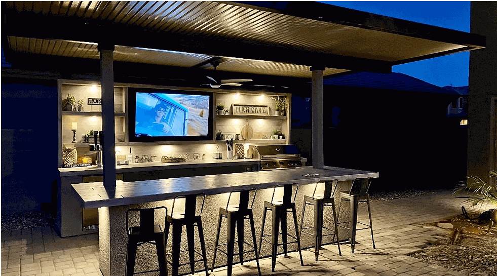 Fantasy Island 20'x20' outdoor kitchen with 70" TV, bar seating, aluminum roof with fan, professional grill, kegerator, and bar lighting at night